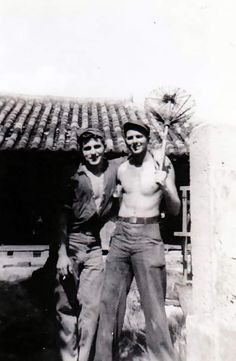 two men standing next to each other in front of a building with roof tiles on it