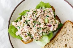 a white plate topped with a sandwich and lettuce covered in chicken salad next to a slice of bread