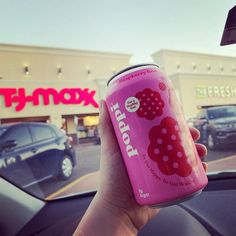 a person is holding up a pink soda in front of a store with cars parked on the street