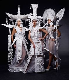 three women in white dresses standing next to each other with paper sculptures on their heads