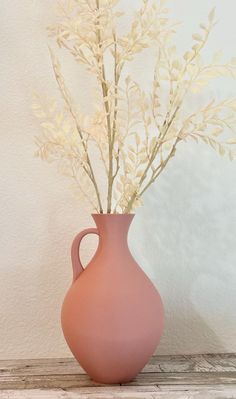 a pink vase filled with white flowers on top of a wooden table next to a wall