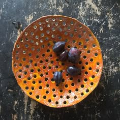 an orange plate with some fruit in it on a table next to a black surface