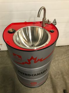 a red and gray metal sink sitting on top of a cement floor next to a white wall