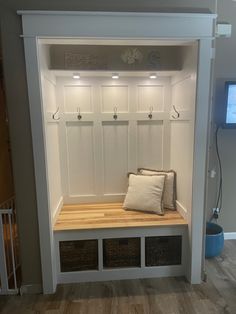 a white bench with some baskets underneath it and a tv on the wall behind it