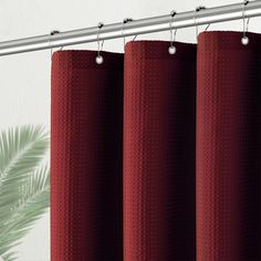 red curtains hanging on a metal rod in front of a white wall and palm tree