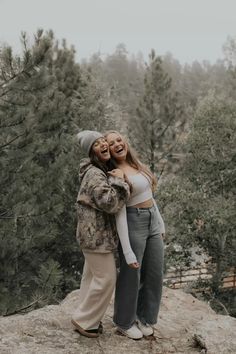 two women hugging each other on top of a hill with trees in the back ground