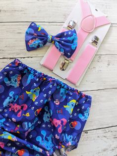 a bow tie and matching shorts are laid out on a white wooden floor next to a pair of pink suspenders