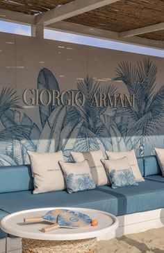 a blue couch sitting under a wooden roof next to a wall covered in palm leaves