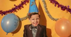 a young boy wearing a party hat and standing in front of balloons