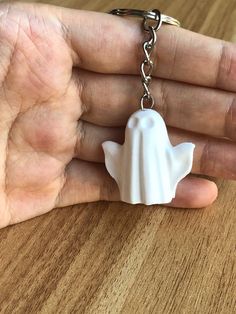 a hand holding a white ceramic keychain with a shell on it's side