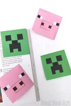 some paper cut out to look like minecraft creeper faces on top of an open book