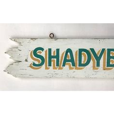 a wooden sign that says shadye hanging from the side of a white wall with green and yellow letters