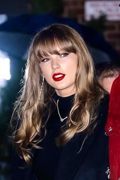 a woman with long blonde hair and red lipstick is standing in front of an umbrella