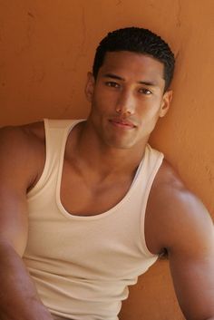 a man leaning against a wall wearing a tank top