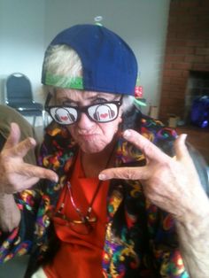 an old woman wearing glasses and a hat making the peace sign with her hands in front of her face