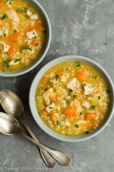 two bowls of chicken and rice soup with spoons next to it on a gray surface