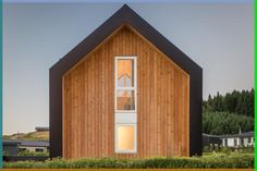 a wooden house with two windows on the front and side, surrounded by greenery