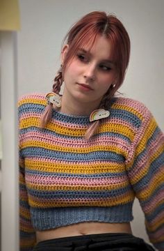 a woman with red hair wearing a multicolored sweater and black pants, sitting in front of a mirror