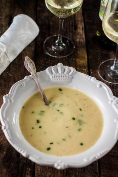 a white bowl filled with soup next to two wine glasses and napkins on a wooden table