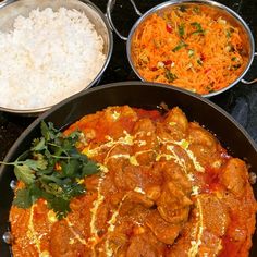 three pans filled with food on top of a black counter next to rice and carrots