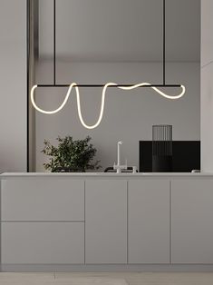 a modern kitchen with white counter tops and lights above the countertop, along with a potted plant