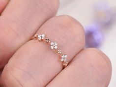 a woman's hand holding a gold ring with five small white flowers on it