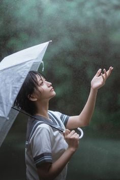 a boy holding an umbrella in the rain with his hand out to catch it up