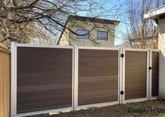 a brown and white fence in front of a house with two garage doors on each side