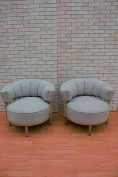 two chairs sitting next to each other on top of a hard wood floor in front of a brick wall