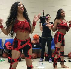 two women dressed in red and black dancing with basketballs on the floor behind them