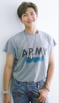 a young man standing next to a white wall wearing a gray army t - shirt