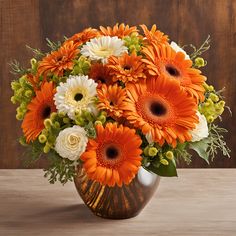 an orange and white flower arrangement in a vase on a wooden table with wood background