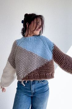 a woman in jeans and a sweater is holding her hands out to the side while standing against a wall