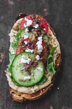 a sandwich with cucumber, tomatoes and feta cheese on it sitting on a table