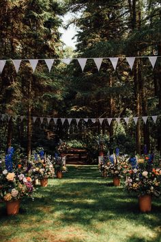 an outdoor ceremony setup with flags and flowers in pots on the grass, surrounded by trees