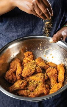 a person is sprinkling seasoning on some food in a metal bowl,