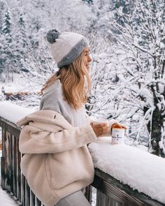 a woman is sitting on a balcony in the snow and holding a cup of coffee