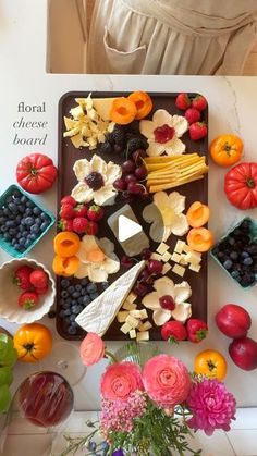 an arrangement of fruits and cheeses on a tray in front of a woman's face