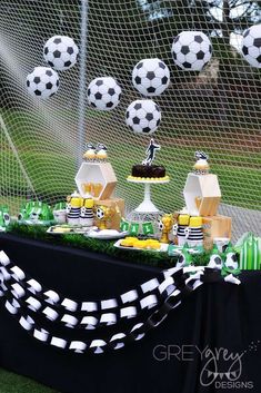 a table topped with lots of desserts and soccer themed decorations on top of a field