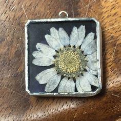 a square pendant with a white flower in the center on a wooden surface, resting on a table