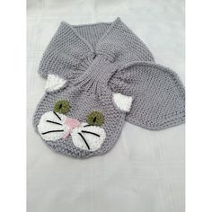 a gray knitted cat hat with ears and tail laying on top of a white sheet