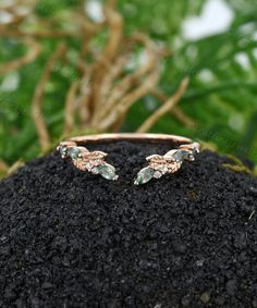 two gold rings with green and white stones on top of a black rock in front of some leaves