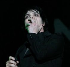 a man holding his hands to his mouth while standing in front of a black background