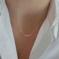 a woman wearing a gold necklace with three small stones on the front and back of her neck