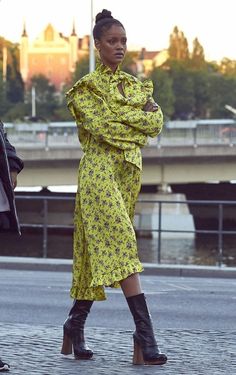 a woman in a yellow dress and black boots is walking down the street with her arms crossed