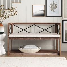 a wooden bench sitting next to a white vase filled with flowers and framed pictures on the wall