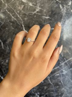 a woman's hand with a diamond ring on top of her left hand, against a marble background