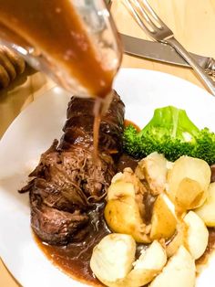 someone is pouring sauce on some meat and potatoes with broccoli in the foreground