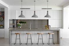 an image of a kitchen with three stools in front of the counter and two lights above it