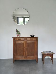 a wooden cabinet sitting next to a table with a mirror on it's wall